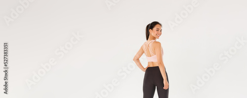 Full length of smiling slim and strong female fitness coach, female athelte in sportswear turn behind to look at camera with pleased, motivated expression, girl ready for workout, white background photo