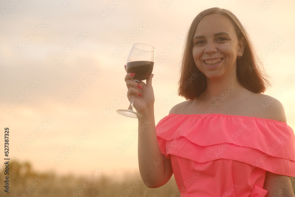 Young woman in bright dress with short hair enjoying fragrance of red wine against sky on sunset. Young woman in bright dress with short hair enjoying fragrance of red wine against sky on sunset.