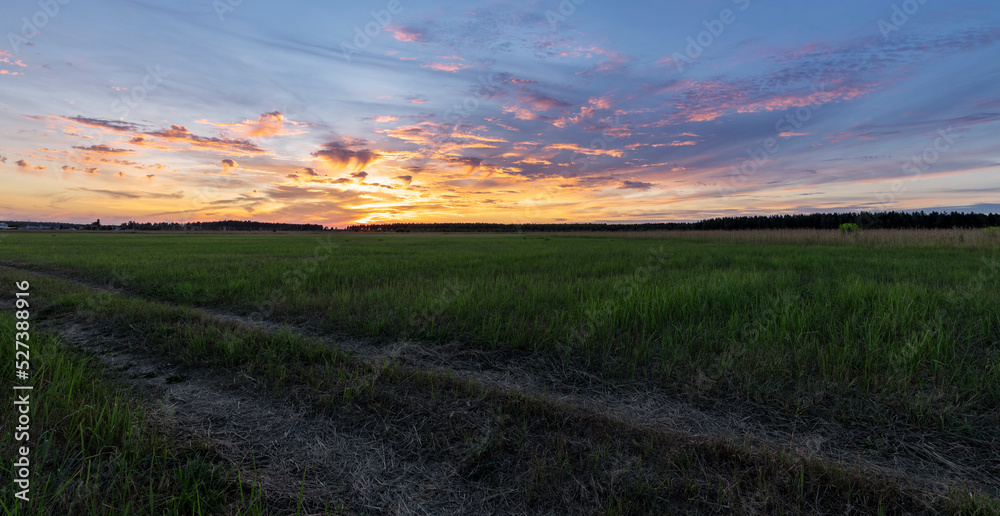 Dirt road in the foreground. Rural landscape with epic clouds and sun on the horizon. Colorful sunset.