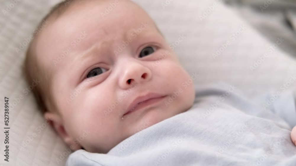 Dissatisfied, crying, upset, sad Newborn baby boy lying in nursery cocoon with blue clothes on bed in bedroom at home, baby morning Dissatisfied, crying, upset, sad Newborn baby boy lying in nursery cocoon with blue clothes on bed in bedroom at home, baby morning