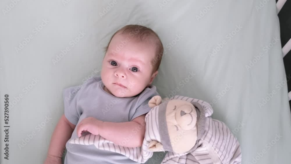 Newborn baby boy 3 months old lies in crib nursery with blue clothes on his back with teddy bear, looks at the camera, happy baby products concept Newborn baby boy 3 months old lies in crib nursery with blue clothes on his back with teddy bear, looks at the camera, happy baby products concept