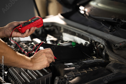 Man using multimeter to measure the voltage of the batteries. Mechanic doing car inspection, he is testing car battery with tester. Check battery voltage with electric multimeter