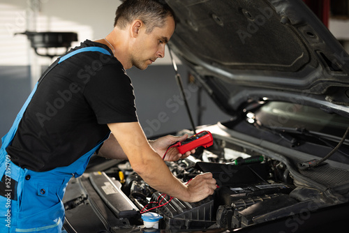 Professional car mechanic check battery voltage with electric multimeter. Automobile diagnosis. Car mechanic repairer looks for engine failure on diagnostics equipment in vehicle service workshop