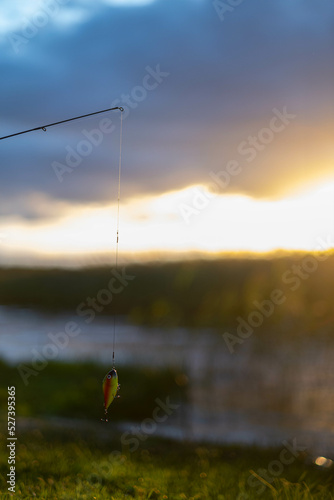 Fishing lure hanging mid air with a beautiful lake and sun blurred background