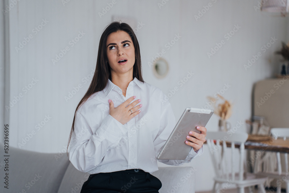 Brunette gorgeous businesswoman in white shirt and black pants rolling eyes touching chest expressing fatigue, annoyance. Pretty student woman making video call by tablet at home. Remote working. Brunette gorgeous businesswoman in white shirt and black pants rolling eyes touching chest expressing fatigue, annoyance. Pretty student woman making video call by tablet at home. Remote working.