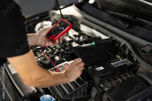 Automobile diagnosis. Car mechanic repairer looks for engine failure on diagnostics equipment in vehicle service workshop. Professional car mechanic check battery voltage with electric multimeter