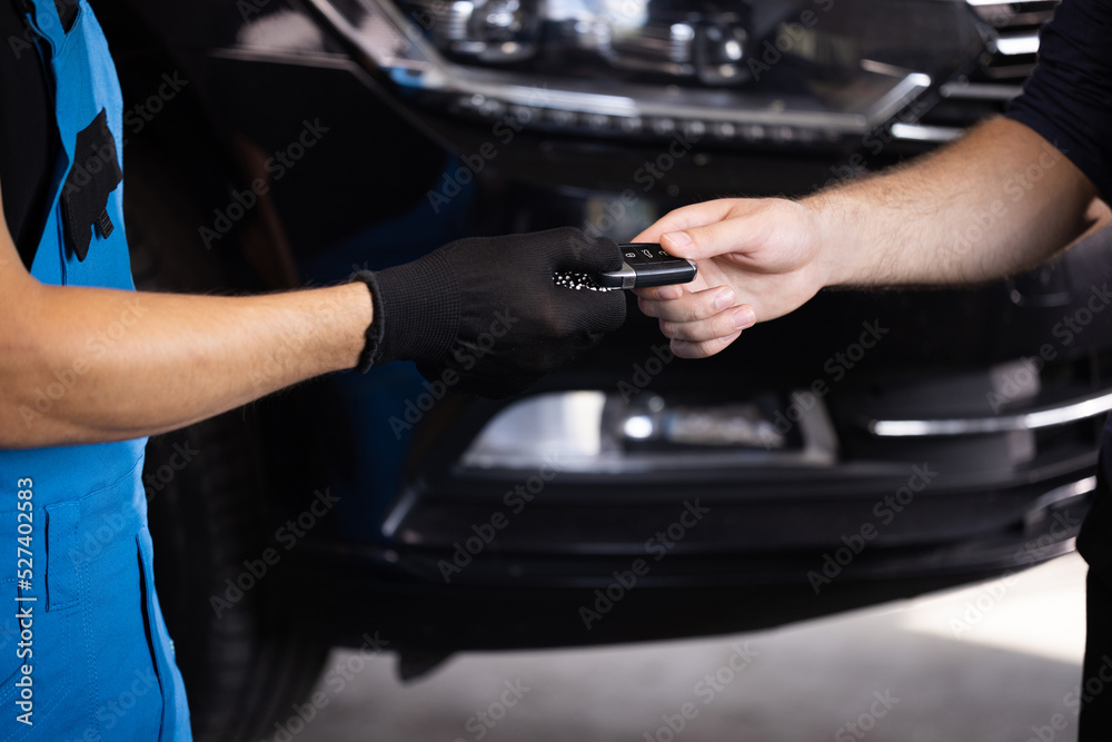 Close up shot of hands of mechanic giving car key to male client after servicing in auto repair shop. Vehicle breaks down. Car repair