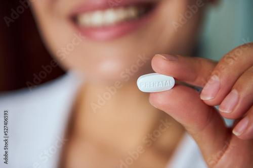 Selective focus on white pill with supplements for pregnant women. Cropped view of blurry happy smiling pregnant woman taking omega 3 vitamin supplement pills. Pregnancy care concept. Prenatal health