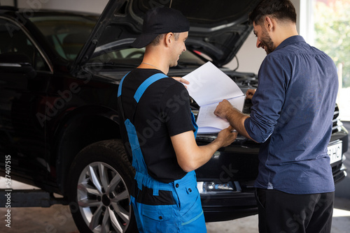 Mechanic and car owner signing paper at workshop. Customer and mechanic discuss upcoming car repair. Auto service, repair, deal and people concept