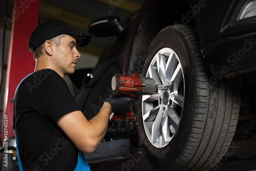 Mechanic is Unscrewing Lug Nuts with Pneumatic Impact Wrench. Repairman Works in a Modern Car Service. Specialists Removes the Wheel in Order to Fix a Component on a Vehicle © uflypro