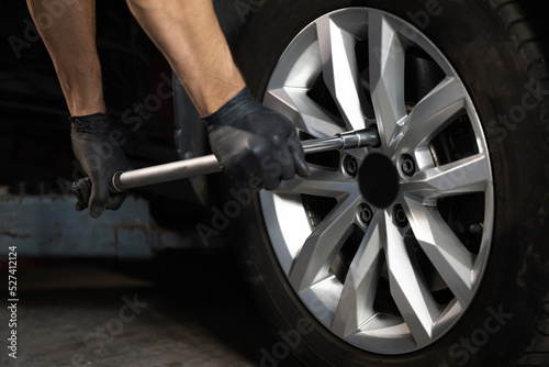 Car mechanic replacing a car wheel tire in garage workshop. Auto service. Repairman mounting wheel tire at service station photo