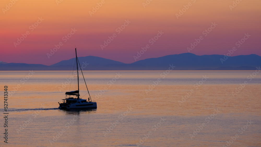 A yacht sailing towards the mountains on the horizon. the sky and the sea are painted red before sunrise. A girl takes a selfie on a yacht.