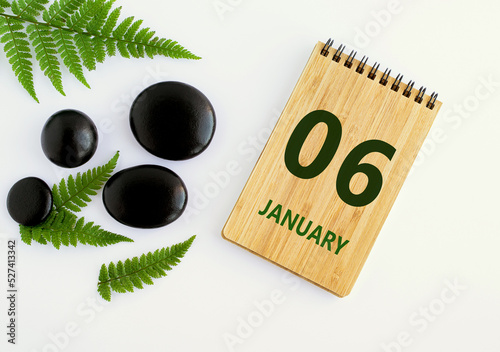 January 06. 06th day of the month, calendar date. Notepad, black stones, green leaves. Winter month, the concept of the day of year