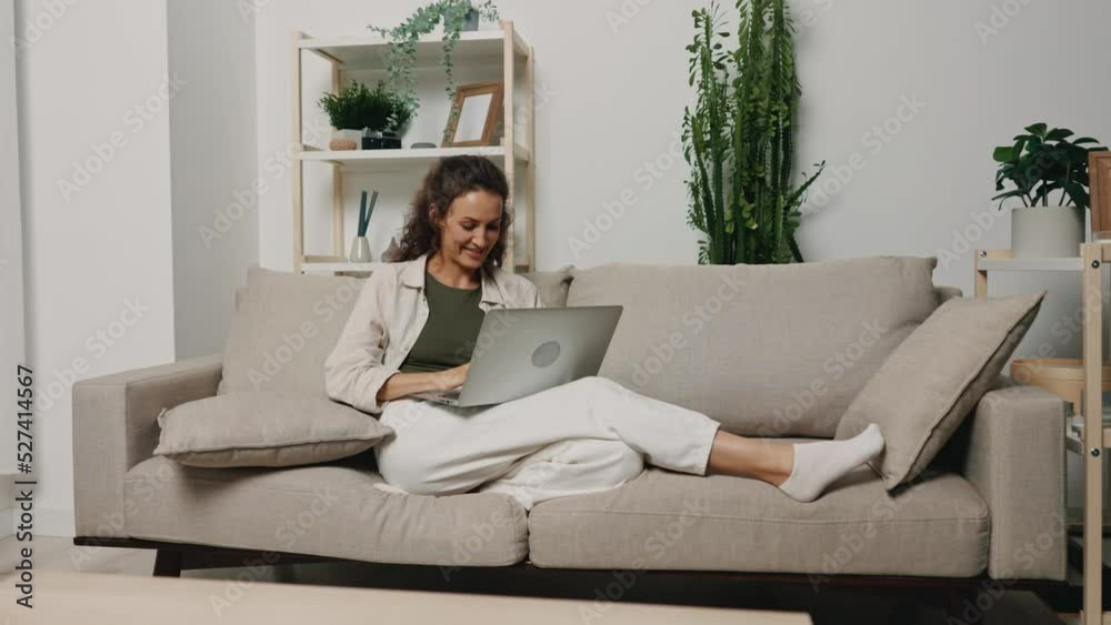 A woman with a laptop lying on the couch at home laughing while watching a movie and relaxing from work A woman with a laptop lying on the couch at home laughing while watching a movie and relaxing from work