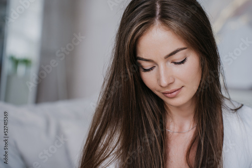 Close up portrait of pretty young woman with loose hair at home looking down, feels shy to share her troubles. Gorgeous Iitalian female with healthy skin. Maternity and women healthcare concept. photo