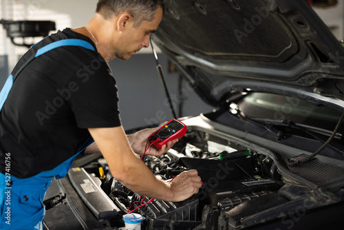 Professional mechanic is working in car service. Good, electrician, electricity, battery charged fully. Check battery voltage with electric multimeter. Car starter battery