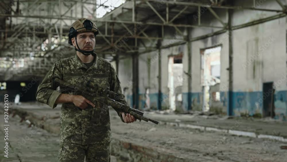 Strong military soldier with big rifle in his hands walking through abandoned old building. Member of armed forces guarding and patrolling destroyed steel factory. Strong military soldier with big rifle in his hands walking through abandoned old building. Member of armed forces guarding and patrolling destroyed steel factory.