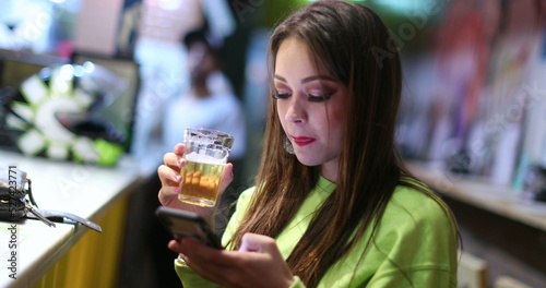 Candid pretty girl at bar drinking beer and checking smartphone