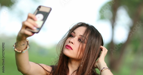 Beautiful young woman taking selfie of herself with phone. Pretty girl takes selfie outside at park