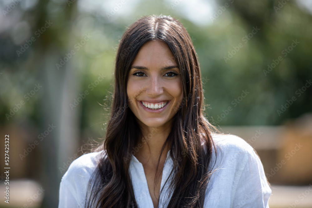 Beautiful young woman smiling while looking at camera standing in the park Beautiful young woman smiling while looking at camera standing in the park