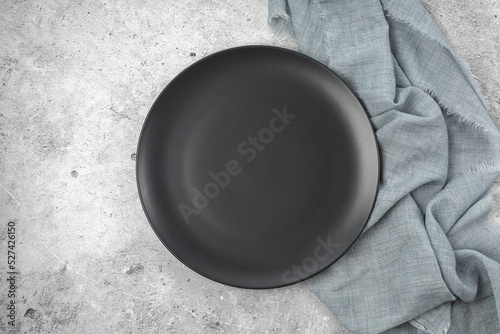 Empty black slate plate on grey stone table and napkin. Food background for menu, recipe. Table setting. Flatlay, top view. Mockup for restaurant menu