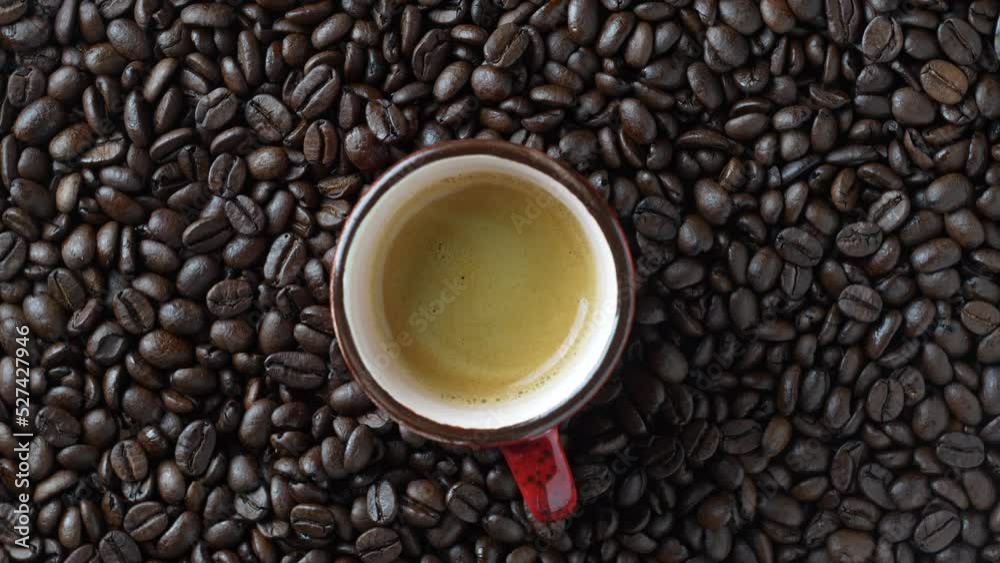 Red cup of hot black coffee with a rotating background of fresh roasted coffee beans, close-up, top view Red cup of hot black coffee with a rotating background of fresh roasted coffee beans, close-up, top view