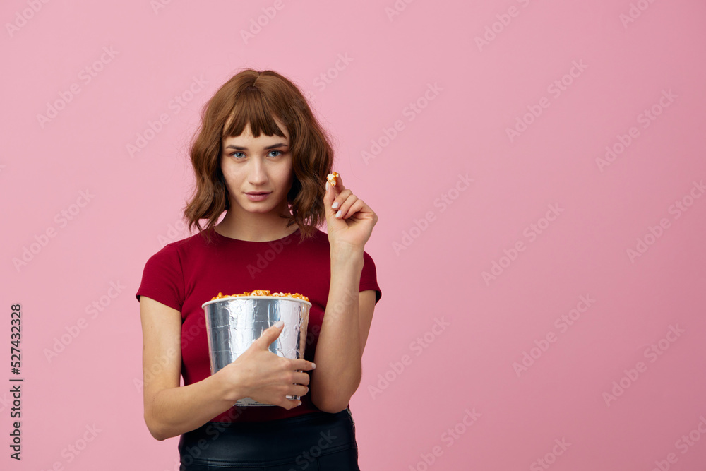 Excited confused cute redhead lady in red t-shirt with popcorn ready for movie evening posing isolated on over pink studio background. Copy space Banner. Fashion Cinema concept. Entertainment offer