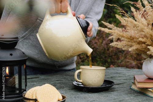 Keep warm, fall tea party. Autumn mood. Female hands pouring tea in mug, drinking tea outdoors.