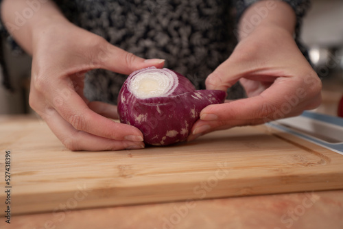 Woman's hands peeling an onion on a wooden board in the kitchen