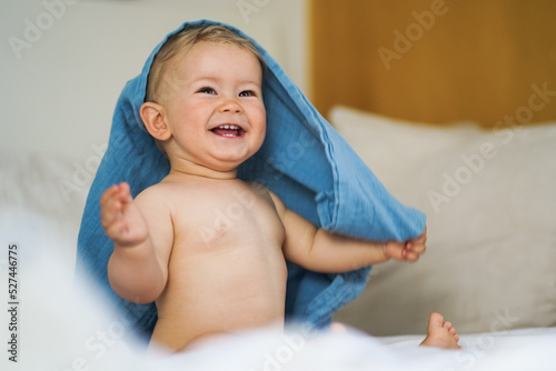 Fotografie mega cute naked almost one year old blond baby boy sitting & laughing at home on
