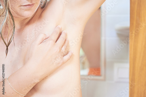 World breast cancer awareness day. A middle-aged woman does a breast self-examination in the armpit with the fingers for any symptoms or lump as a precaution in front of the mirror in the bathroom.