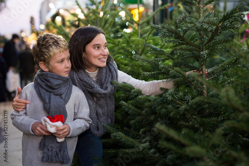 Cute cheerful preteen boy with mother looking for Christmas tree at traditional outdoor fair