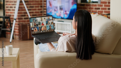 Asian person with portable computer working remotely while having online virtual teleconference. Woman working from home while discussing with manager on digital video call conference.