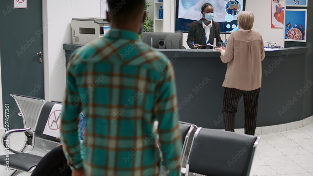 Busy hospital reception with diverse group of people during covid 19 epidemic, waiting to attend checkup appointment with specialist. Waiting room area during coronavirus pandemic.