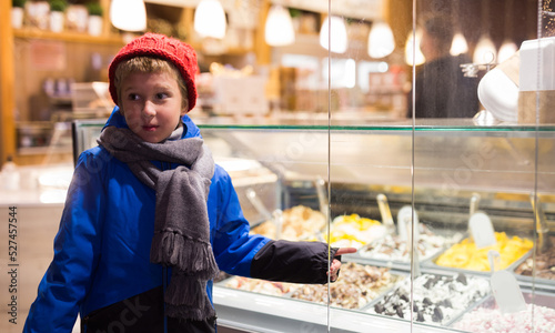 Fotografie Portrait of interested tween boy in warm clothes pointing to ice cream display c