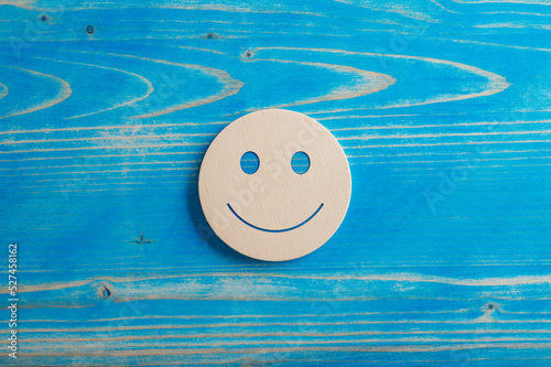 Smiling face expression cut into a wooden circle placed over blue background