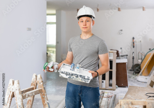 Portrait of a fifteen-year-old teenager with a roller and a paint tray in his hands, working on a construction site in an ..apartment during renovation work photo