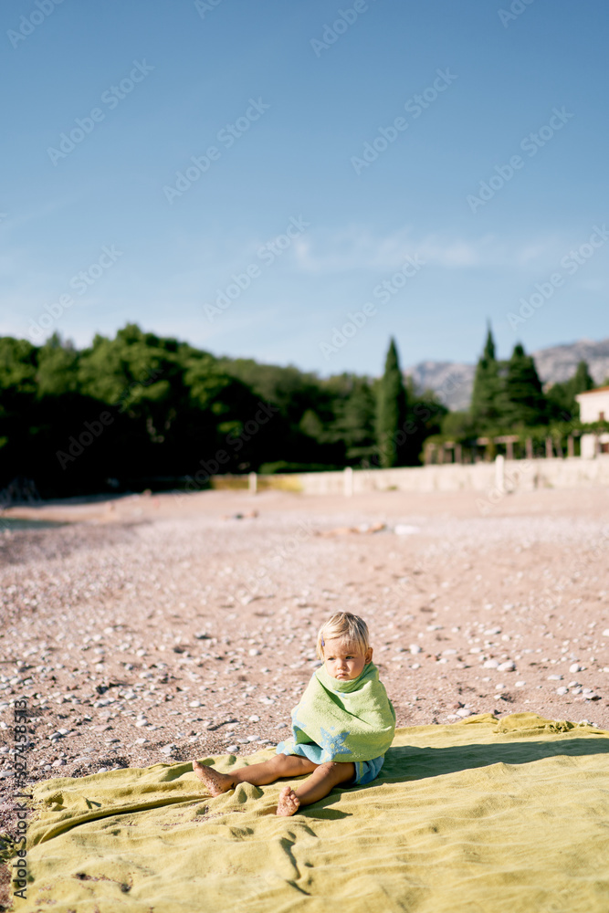 Little girl in a towel sits on the beach. High quality photo