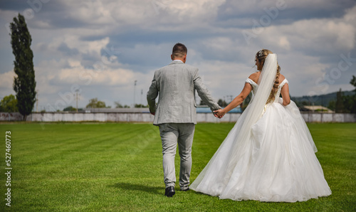 Happily married wedding couple walking hand in hand on the football field. Back view portrait of bride and groom on the soccer pitch. photo