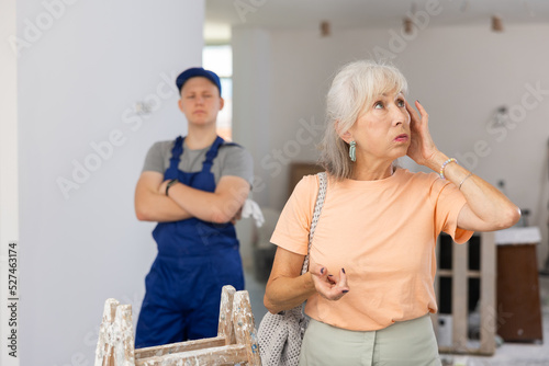 Fotografie Portrait of senior woman making helpless gesture, disappointed by teenage boy she employed for part-time job in construction site