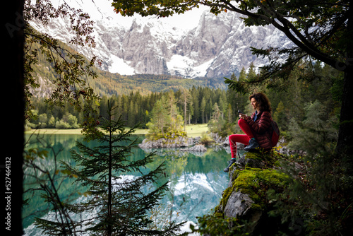 Woman Backpack Tourist Sitting Near An Alpine Lake Using Mobile Phone