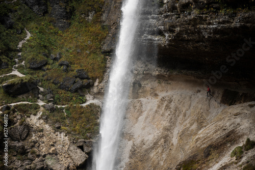Woman Extreme Runner on A Scenic Alpine Footpath Trail Under a Big Waterfall