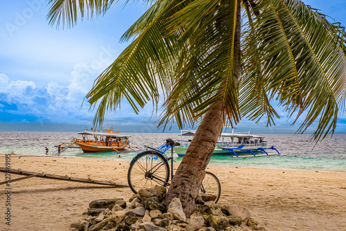 Bicycle by the beach with boats docked that brought tourists and travelers into the island paradise. There is white sand, blue skies, clear waters where people can enjoy and relax and have peace.