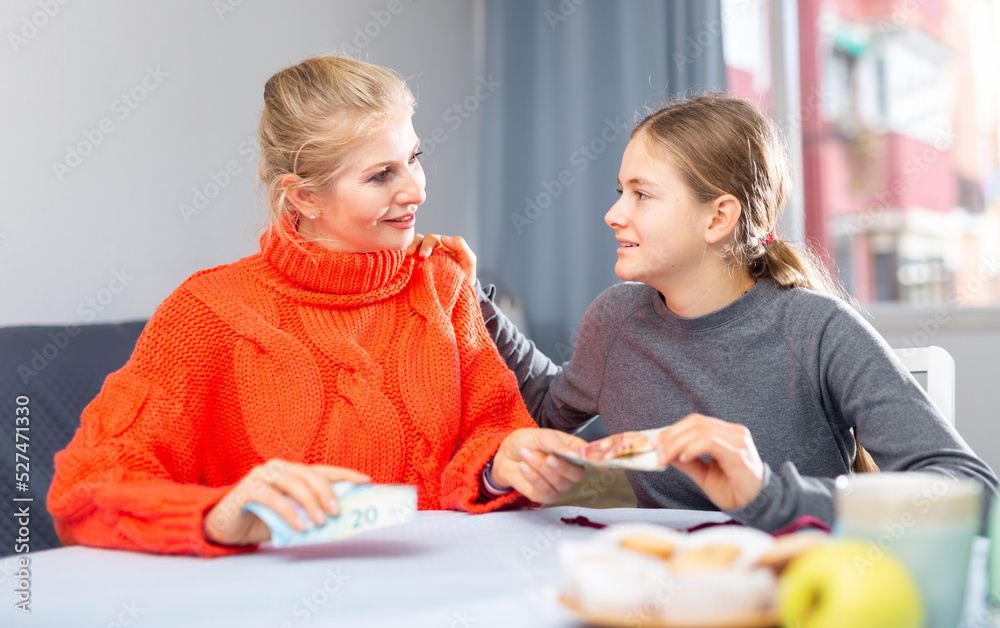 Fototapeta premium Mom gives pocket money to her daughter. Joyful daughter thanks mom