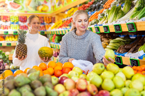 Daughter and mom buy fruit - pineapple and melon at the grocery store