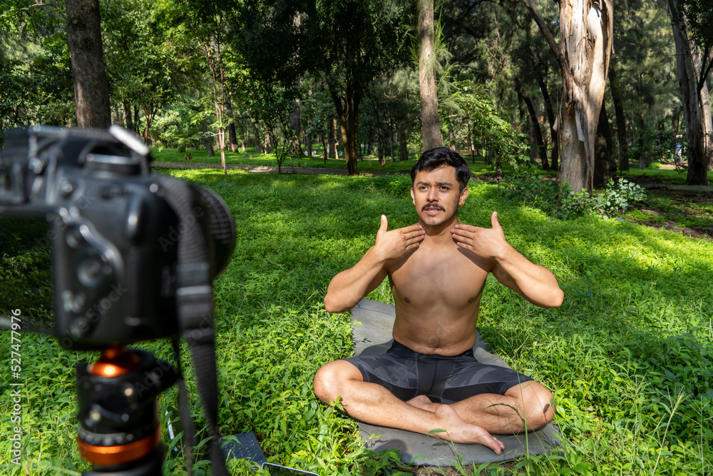 Obraz premium Young man practicing yoga asana, balance, meditating while standing on one leg on sports mat on green grass in park. Using tablet for online class.