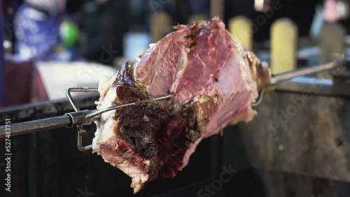 A large piece of meat, pork legs are baked on a skewer. Grilling over an open fire. Street food. Pork leg is cooked on a spit. Beef or pork is cooked until crisp. A popular meat dish.