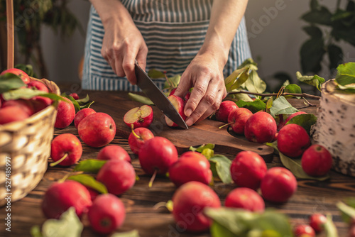 Woman in an apron in the kitchen is cutting appetizing red apples from a fresh harvest. Concept of an autumn cozy atmosphere, cooking dishes from organic healthy apples from own garden