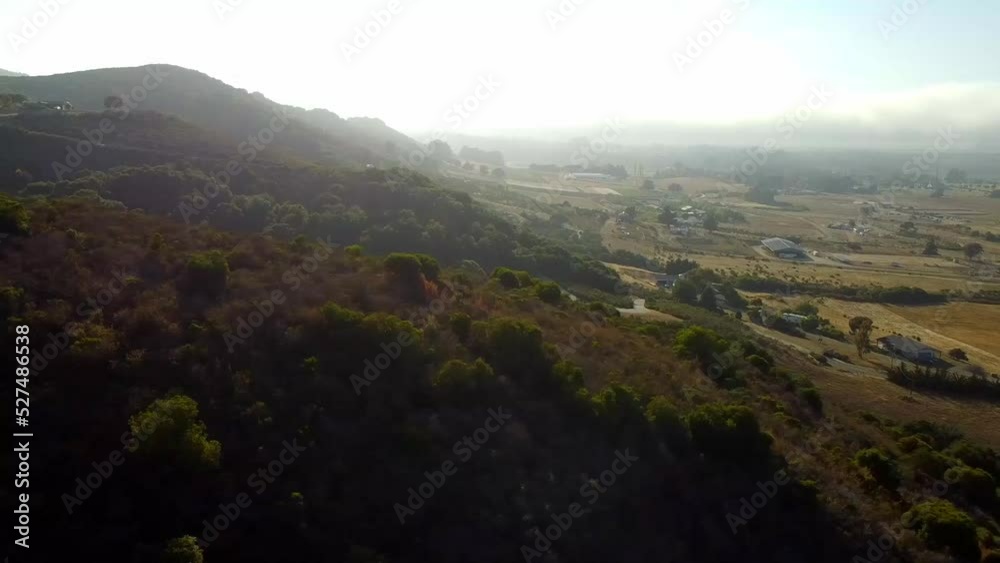 Drone shot over hill with sunshine through fog and farm in the background. Drone shot over hill with sunshine through fog and farm in the background.