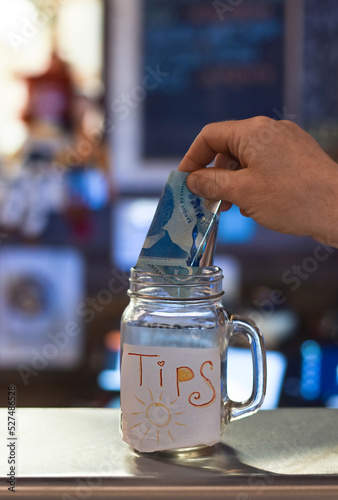 Persons hand putting canadian cash money tips into tips jar at reastaurant photo